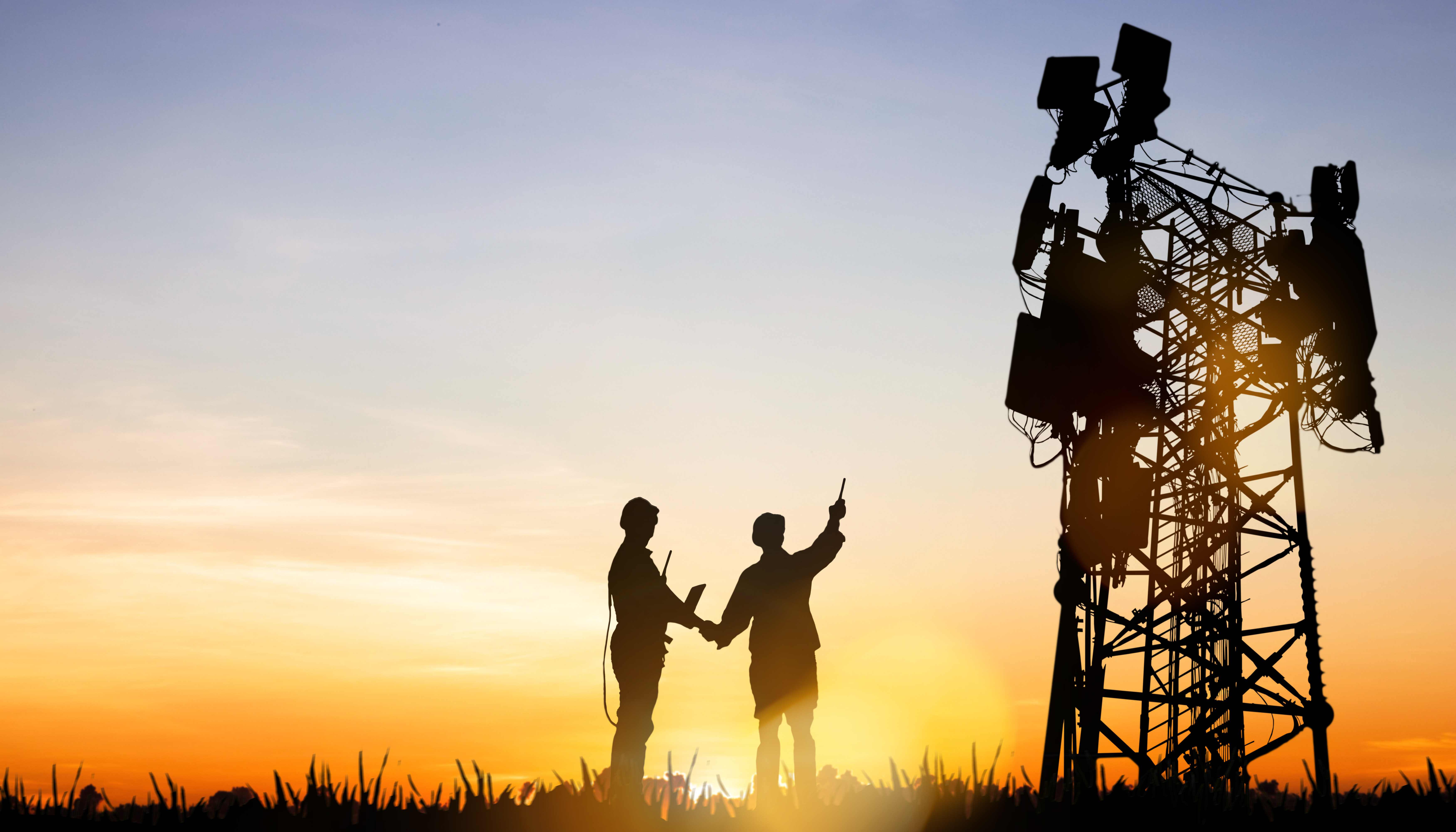 two 5G engineers pointing at cell tower at sunset